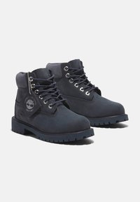 Stivali alla caviglia impermeabili blu navy in pelle scamosciata, caratterizzati da occhielli metallici, lacci rotondi e una suola in gomma robusta con un design testurizzato.