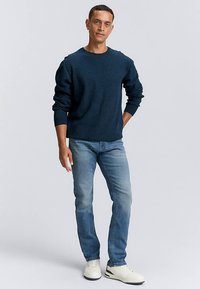 Laivastonsininen neulepusero pitkillä hihoilla, yhdistetty vaaleansinisiin farkkuihin ja valkoisiin tennareihin. Rento istuvuus, teksturoitu kangas, yksinkertainen muotoilu.