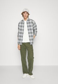 Rutete skjorte i grå og grøn over en hvid T-shirt, parret med olivengrønne cargo-bukser og hvide sneakers, toppet med en grå kasket.