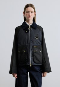 Μαύρο αδιάβροχο μπουφάν με γιακά από κοτλέ ύφασμα, φερμουάρ μπροστά, δύο μεγάλες τσέπες, χρυσές μεταλλικές λεπτομέρειες και λογότυπο.