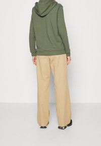 Zelená mikina s kapucí na šňůrku a žebrovanými manžetami, v kombinaci s béžovými širokými kalhotami. Tento outfit má ležérní a pohodlný design.