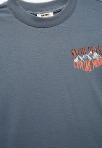 Katoenen T-shirt in leisteenkleur. Kenmerkt een vooropdruk met bergen en de tekst "SNOW PEAK EXPLORE MORE" in oranje. Geribbelde halslijn.
