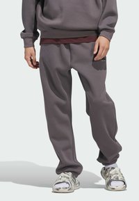 Grauer Pullover und Jogginghose aus weichem Material; lockere Passform mit elastischen Bündchen; kombiniert mit gemusterten Slippern in Weiß und Grau.