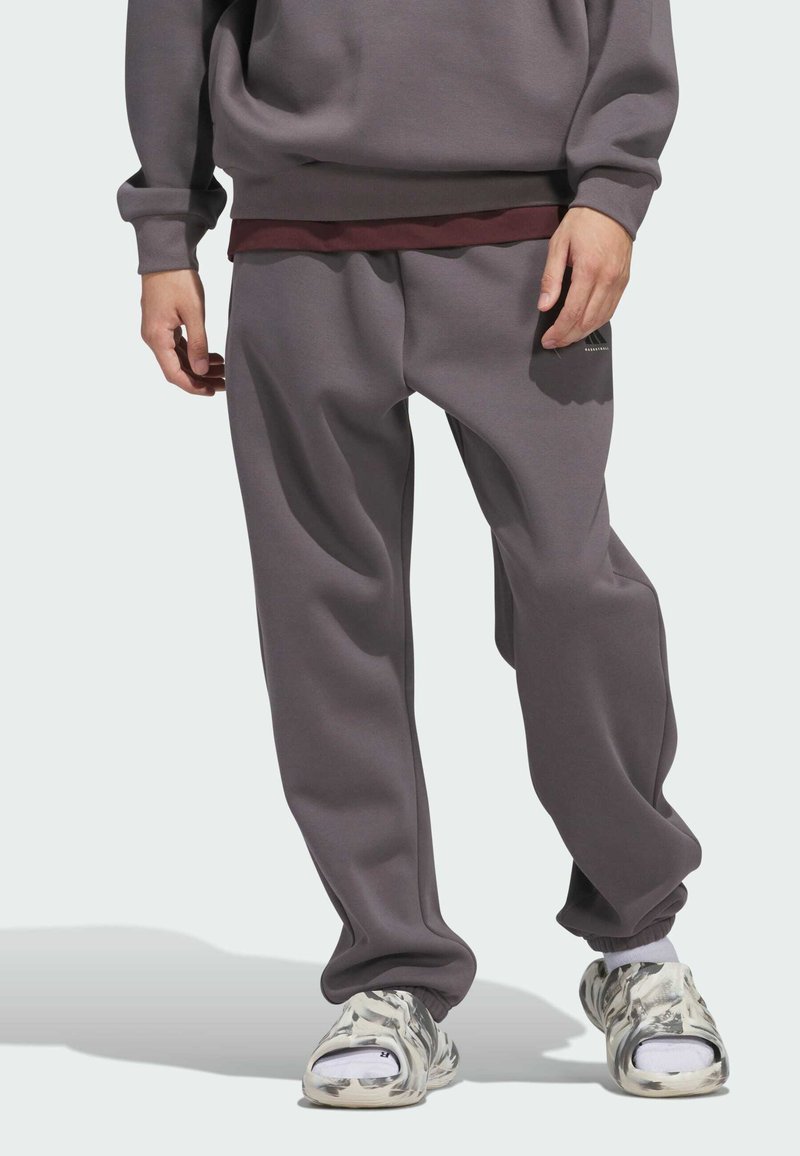 Grauer Pullover und Jogginghose aus weichem Material; lockere Passform mit elastischen Bündchen; kombiniert mit gemusterten Slippern in Weiß und Grau.