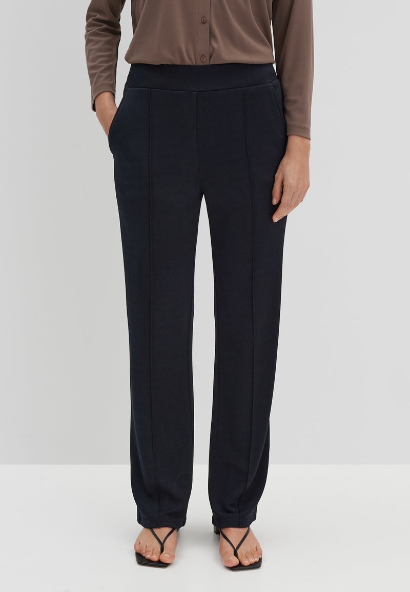 Navigatieblauwe, gladde stoffen broek met recht gesneden ontwerp, elastische tailleband en zijzakken. Gestyled met een lichtbruine overhemd met knopen en zwarte sandalen.