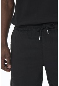 Black jogger pants made of soft fabric with an elastic waistband, adjustable drawstring, and side pockets. Smooth texture, casual design.