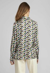 Chemise à manches longues avec un motif chevron coloré en vert, rose, bleu et noir. Tissu lisse avec un col classique et des poignets boutonnés.