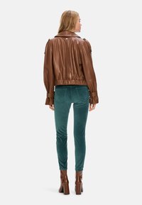 Brown leather jacket with gathered waist and cuff details, paired with teal velvet pants and brown heeled boots. Back view.