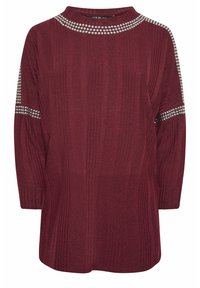 Bordeaux stickad topp med långa ärmar, ribbat mönster och silverdetaljer längs halsringningen och ärmarna. Rund halsdesign.