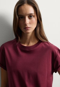 T-shirt bordeaux in cotone morbido con collo rotondo e maniche corte, caratterizzato da una texture liscia e una vestibilità comoda.