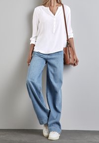 Chemisier blanc à boutons avec col en V, associé à un jean à jambes larges bleu clair. Accessoirisé d'un sac à main marron et de baskets blanches.