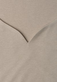 Gros plan d’un tissu beige avec un détail de couture en forme de V créant un motif texturé subtil.