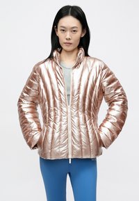 Fémes rózsaszín színű puffertalpú dzseki vízszintes steppelt mintázattal, magas gallérral és elől cipzárral. Szürke inggel és kék nadrággal párosítva.