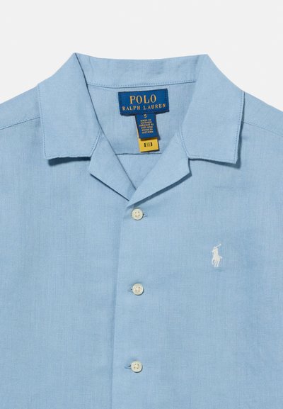 Chemise bleu clair à col avec boutons blancs, étiquette Polo Ralph Lauren, et logo joueur de polo brodé blanc sur la poitrine.
