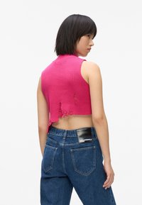 Rozā, īsā adīta blūze ar augstu apkakli, ar nolietotiem galiem un neapstrādātu apakšmalu. Apvienota ar augsto jostu džinsu biksēm, kurām ir logotipa uzlīme.