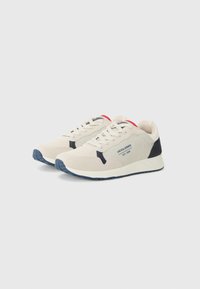 Beige athletic shoes with navy accents, suede and mesh material, round toe, laces, logo on the side, red detailing on the heel.