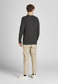 Mörkgrå långärmad skjorta med ribbade manschetter, i kombination med ljusbeige skräddarsydda byxor och vita sneakers med svarta detaljer.