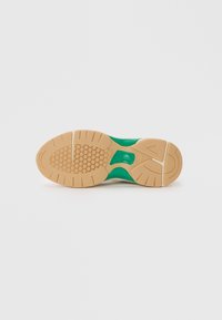 Green and beige athletic shoe sole with a textured rubber design, featuring hexagonal patterns and a raised logo detail.