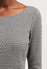 Robe noire et blanche présentant un motif géométrique en losange, avec un col rond et des manches longues, confectionnée dans un tissu lisse et texturé.