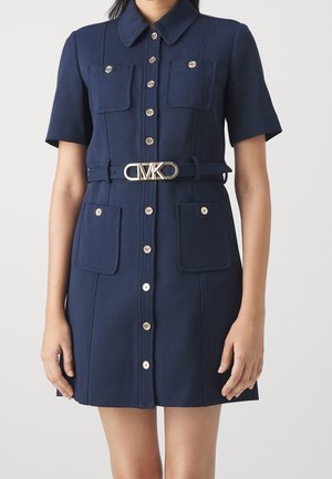 Robe bleu marine à manches courtes avec col, fermeture à boutons sur le devant, deux poches poitrine et deux poches hanches, et ceinture avec boucle logo MK dorée.