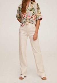 Blouse courte à manches courtes à fleurs avec un devant noué, associée à un pantalon beige taille haute à jambes larges et des sandales plates.