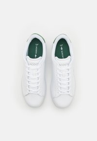 Sneakers bianchi con punte rotonde, lacci piatti e accenti verdi sulla linguetta e sul retro. Presentano una soletta ortolite e un logo del marchio sul lato.