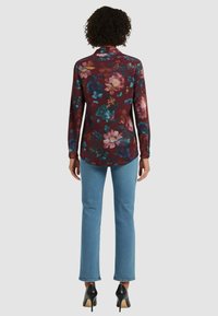 Camicia a maniche lunghe color borgogna con vivace stampa floreale, abbinata a jeans azzurri chiari e tacchi neri. Tessuto liscio con orlo arrotondato.