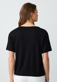 Zwarte katoenen T-shirt met een relaxte pasvorm, korte mouwen en een wijde halslijn. Naadtoeslag langs de randen en een gladde textuur.