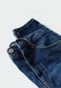 Jean en denim bleu foncé plié avec poche avant visible, passants de ceinture, bouton et surpiqûres orange sur fond blanc.