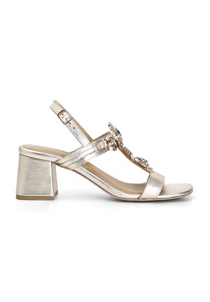 Sandal con tacco a blocco in metallo dorato, con cinturino alla caviglia regolabile e decorazioni di gioielli sugli strappi anteriori. Texture liscia.
