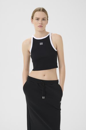 Svart ribbet crop-top med hvit sporty hals, med en liten logo. Kombinert med svart skjørt med snøring og sidelommer.
