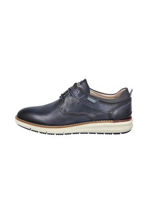 Zapato casual de hombre en piel azul oscuro con cordones, suela blanca y detalles cosidos, visto desde el lado exterior sobre un fondo blanco.