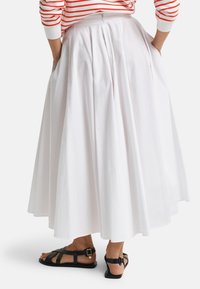 Persona che indossa una gonna midi plissettata bianca, una maglietta a manica lunga a righe rosse e bianche e sandali neri piatti con fibbie.