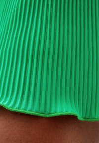 Zelená ribovaná tkanina s hladkým povrchem. Spodní okraj je dokončen kontrastním švem, který zvýrazňuje živou barvu a výrazný vzor.