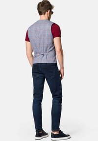 Szary kamizelka w kratę z dopasowanym tyłem i regulowanym paskiem, w zestawieniu z ciemnoniebieskimi dżinsami i czarnymi trampkami, widoczna z tyłu.