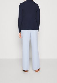 Námořnictvem modrý žebrovaný svetr s nahrnutým límcem, kombinovaný se světle modrými širokými kalhotami. Tento outfit má uvolněný střih a hladkou texturu.