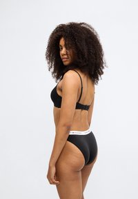 Σετ μαύρο σουτιέν και ψηλόμεσο σλιπ. Το σουτιέν διαθέτει ρυθμιζόμενες τιράντες· το σλιπ έχει λευκή μέση με λογότυπο. Λείο, ελαστικό ύφασμα.