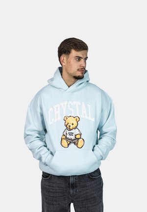 Haut à capuche bleu clair en tissu doux, orné d'un graphique d'ours avec le texte "Crystal Paris", doté d'une grande poche avant et d'une capuche avec cordon de serrage ajustable.