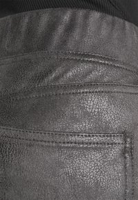 Svart lädertextil med en texturerad yta och synliga stygn; inkluderar en fickdetalj sydd på baksidan.