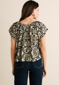 Haut noir et crème à motifs avec manches volumineuses, présentant un col froncé et un tissu texturé, associé à un jean en denim foncé.