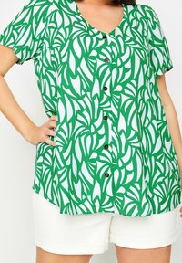 Green and white short-sleeve shirt with a leaf pattern, featuring a V-neck and brown buttons down the front. Paired with white shorts.