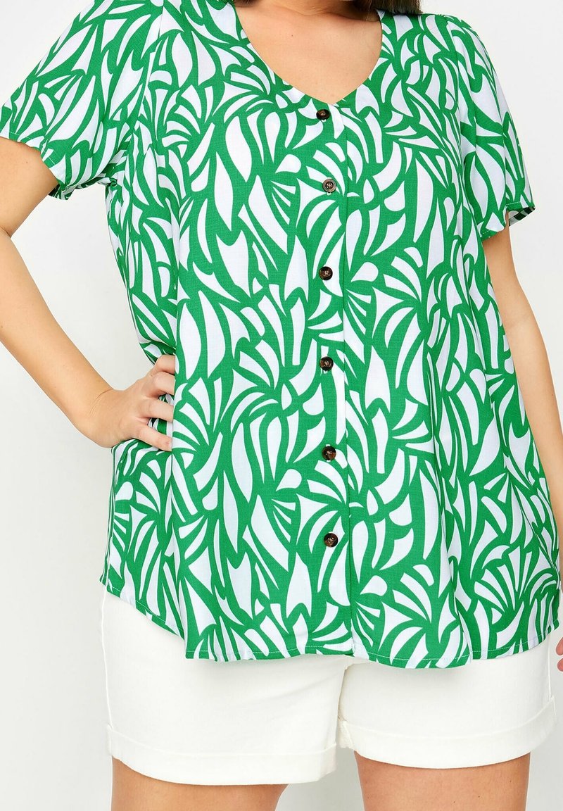 Green and white short-sleeve shirt with a leaf pattern, featuring a V-neck and brown buttons down the front. Paired with white shorts.