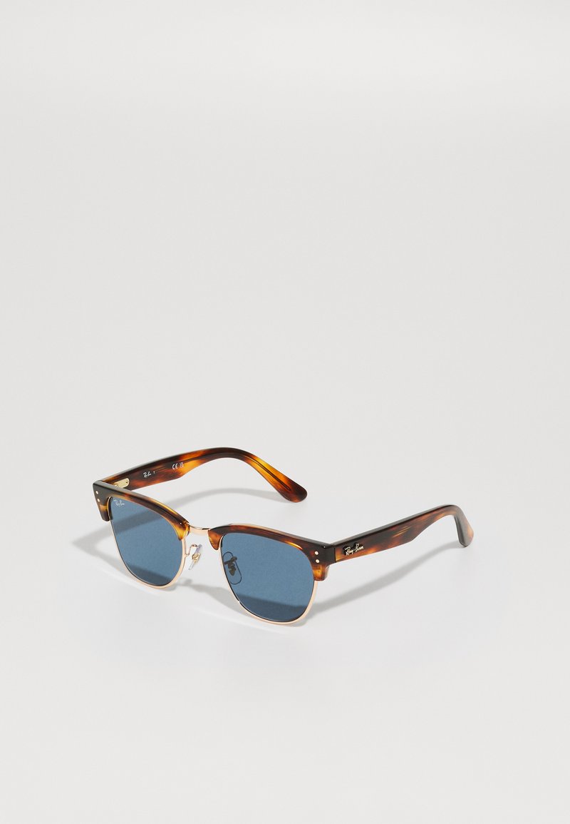 Ochelari de soare din scoică de broască țestoasă, cu lentile albastre, punte metalică și suporturi transparente pentru nas. Logo-ul iconic Ray-Ban pe braț. Formă unghiulară.