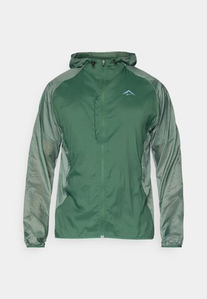 Veste légère verte avec une fermeture éclair intégrale, une capuche réglable et des manches texturées contrastantes. Comprend un petit logo sur la poitrine.