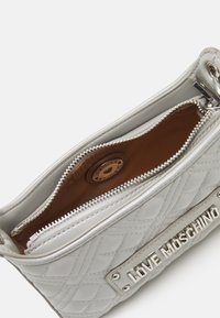 Sac à main en cuir matelassé argenté avec un plaque en relief "LOVE MOSCHINO", doté d'un compartiment principal zippé et d'un intérieur en tissu brun.