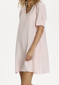 Světle růžové šaty vyrobené z hladkého materiálu, s výstřihem do V, krátkými nabíranými rukávy a celoplošným tečkovaným vzorem. Mírně volný střih.