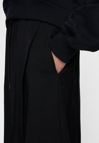 Felpa nera con polsini a costine, dotata di tasca frontale e pantaloni jogger neri abbinati con un discreto logo 10 e design plissettato.