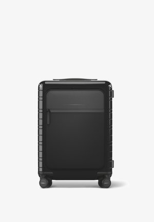 Black hard-shell suitcase with a smooth texture, zipper pocket on front, horizontal accents, and four spinner wheels for mobility.