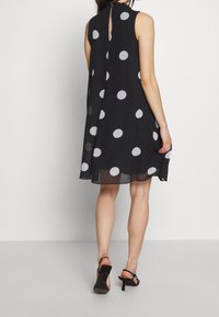Svart klänning med stora vita prickar, ärmlös design, genomskinligt tyg, nyckelhål bakdetalj och en utsvängd silhuett.