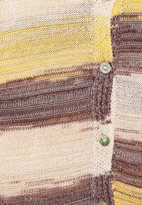 Gros plan d’un tissu tricoté avec des rayures horizontales jaunes, brunes et crème et trois boutons ronds et brillants.
